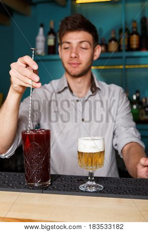 Barman in bar interior stir ice in red berry alcohol cocktail. Professional bartender at work in night club. Service industry occupation. Vertical image