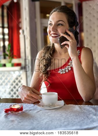 The girBeautiful girl in a red dress in a cafe talking on the phonel in the cafe