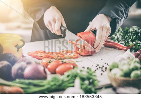 The chef prepares the meal, cuts pepper with a chef's knife.