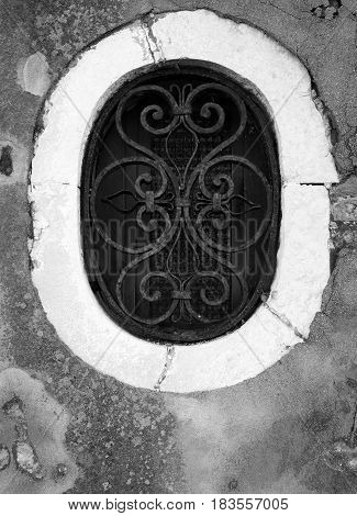 Ornate old oval window in venice with rusting metal grill and brickwork