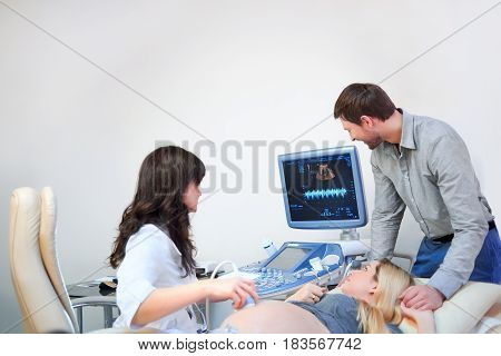 Happy mature man supporting his pregnant wife holding her hand during sonogram procedure at the fertility clinic copyspace doctor professionalism technology ultrasound scanning medicine health.