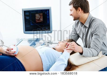 Cropped shot of a loving man holding hand of his pregnant wife during medical examination ultrasound scanning sonogram technology pregnancy expecting fertility family support love healthcare concept.
