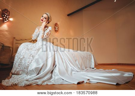 The bride in a white dress sitting on a bed in her room.