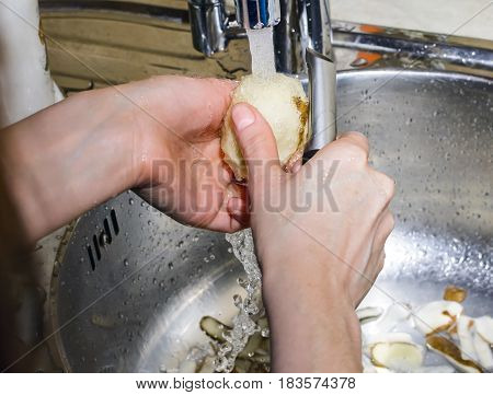 Woman peeling potatoes in the sink under running water