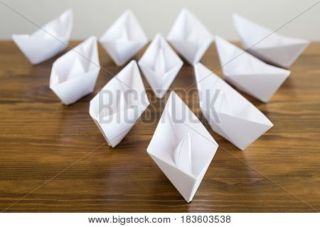 Origami white paper boats on a wooden table, soft focus.
