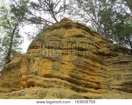 Colorful sandstone and limestone rock cliff or outcrop along the trail to St. Louis Canyon at Starved Rock State Park with trees in spring.