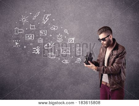 An elegant hipster guy trying to use a vintage camera with camera settings icons drawn on wall, like flash, white balace or ISO value concept