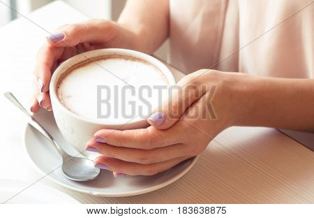 A beautiful young woman sitting in a cafe. Girl drinks Cappuccino.