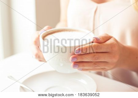 A beautiful young woman sitting in a cafe. Girl drinks Cappuccino.