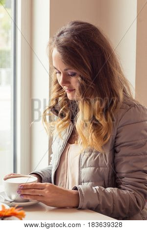 A beautiful young woman sitting in a cafe. Girl drinks Cappuccino.