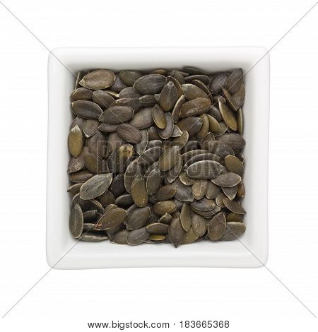 Pumpkin seeds in a square bowl isolated on white background