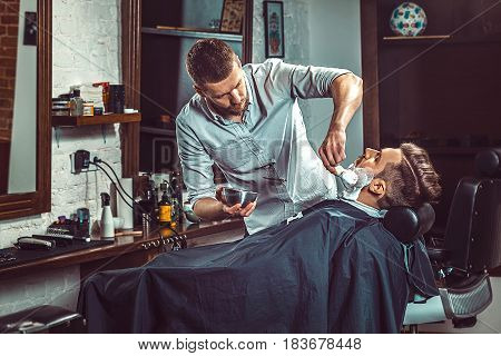 Hipster client visiting barber shop. The hands of young barber making the cut of beard