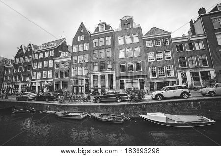 Amsterdam - October 2014, Netherlands: Typical street of the old Amsterdam center with cars parked near traditional houses and boats in canal, black and white photo