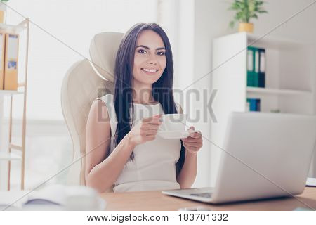 Young Attractive Business Lady Is Having A Cup Of Coffee At Her Workplace. She Is Happy And Thinking