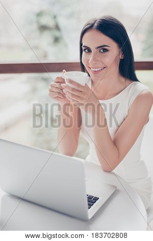 Cute Young Brunette Is Having Tea At The Cafe. She Is Happy, Smiling. Her White Outfit Is Very Smart