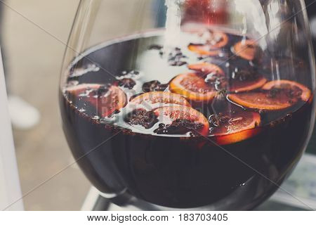 Making hot alcohol, mulled wine for sale at country fair. Glintwine from red wine with citrus and cloves in big glass, Closeup