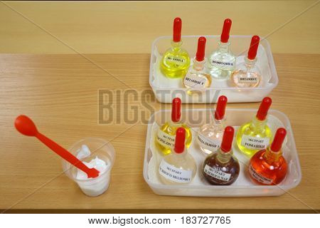 Test tubes with solutions on table, glass with cream and spatula, Text translation - sea buckthorn oil, almond oil, green tea extract, oatmeal extract, vitamin A, E, F, B5