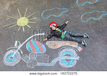 Happy kid boy in race helmet having fun with motorcycle picture drawing with colorful chalks. Children, lifestyle, fun concept. Creative leisture for kids