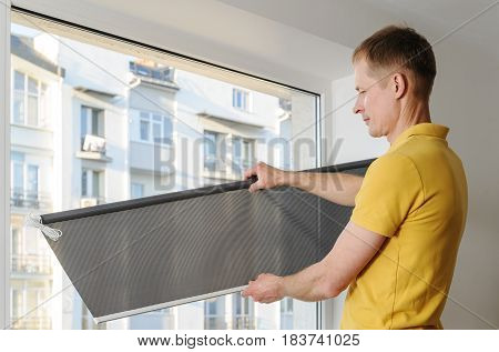 Man is holding fabric window blind gray.