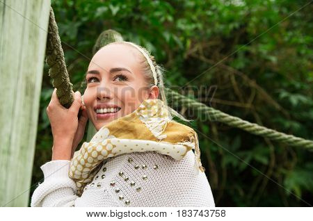Close up shot if young smiling blond girl sitting in a walking wooden bridge looking peaceful