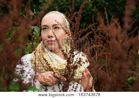 Close up portrait of beautiful young blond woman behind some red forest weeds