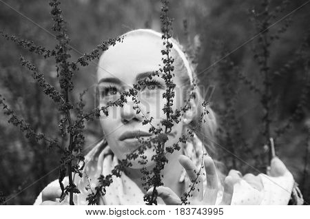 Close up black and white portrait of beautiful young blond woman behind some red forest weeds