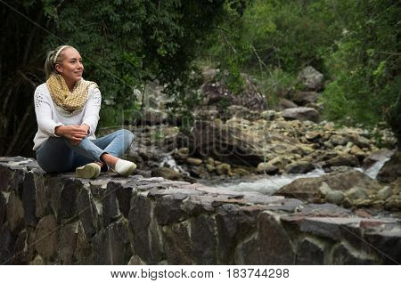 Attractive young woman sitting in a cold forest by the river enjoying the view
