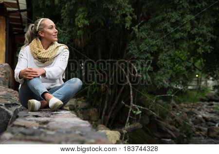 Attractive young woman sitting in a cold forest by the river enjoying the view