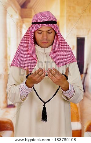 Cute young arabian guy praying to god while holding a masbaha.