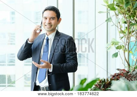Business man talking smart phone with happy smiling face standing by windows inside eco office building background businessman on smart phone