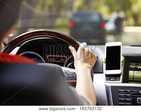hand of a female holding the steering wheel of a vehicle with a cellphone mounted on the dashboard.