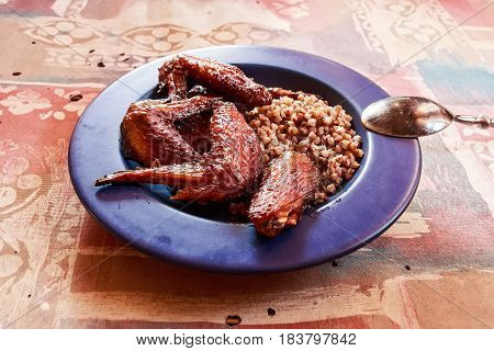 Close up tasty cooked chicken wings and boiled buckwheat on blue plate