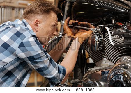Being careful. Gifted successful diligent serviceman using special tool for drawing up a bolt on his bike while repairing it