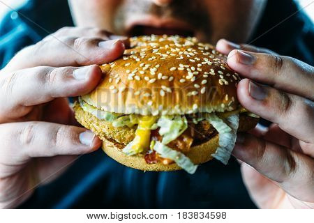 Hungry fat man holds hamburger and going to bite fas food. Unhealthy food concept