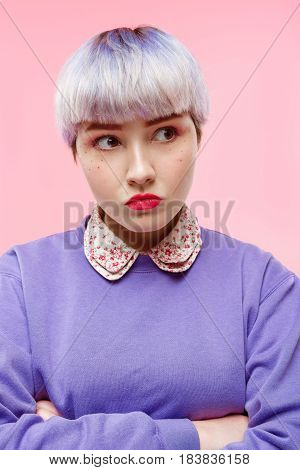 Fashion close-up portrait of angry beautiful dollish girl with short light violet hair wearing lilac sweater over pink background. Copy space.