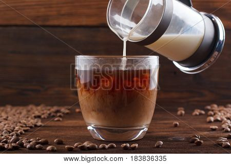 Coffee With Milk In A Transparent Cup. Milk Is Poured Into Coffee On A Wooden Background