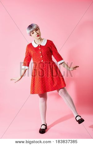 Picture of beautiful dollish girl with short light violet hair wearing red dress over pink background. Copy space.