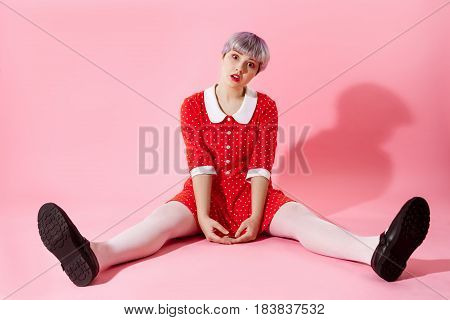 Picture of beautiful dollish girl with short light violet hair wearing red dress over pink background. Copy space.