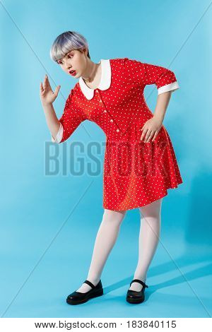 Picture of beautiful dollish girl with short light violet hair wearing red dress over blue background. Copy space.