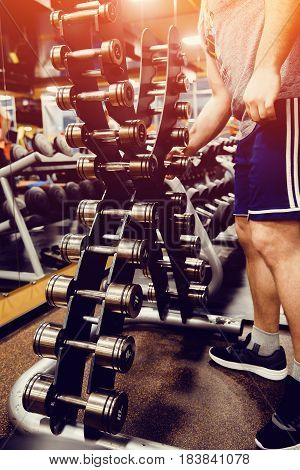 Sports equipment dumbbell rests in a row. man takes a dumbbell. high contrast and monochrome color tone.