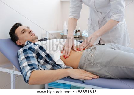 In the clinic. Handsome nice pleasant man lying on the medical bed and being examined by the doctor while being at the hospital
