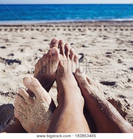 closeup of the feet of two young men playing footsie on the beach, with the sea in the background