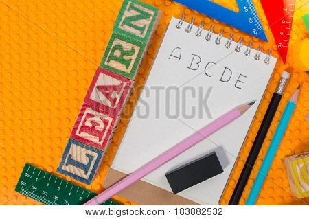 Blank notebook with word ABC and school supplies on yellow plastic brick plate. Learning background concept.