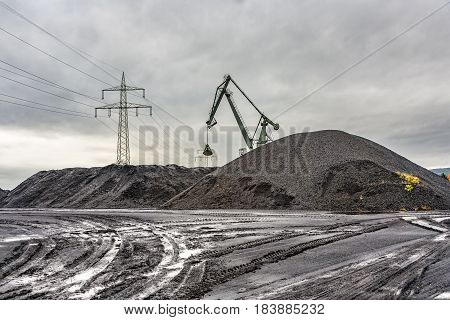 bagger at a huge charcoal hill with pylon in background