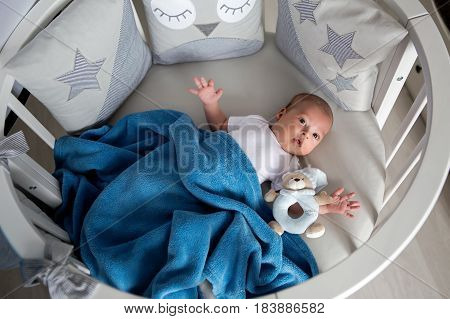 Newborn boy lies in a round bed on his back with a rattle