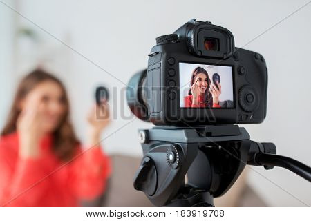 blogging, technology, videoblog and people concept - happy smiling woman or beauty blogger with eyebrow pencil, mirror and camera recording makeup  tutorial video at home