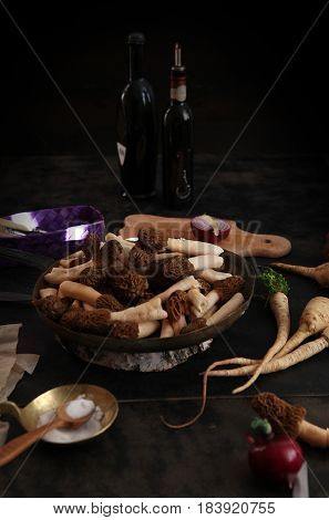 still llife with raw morels in the copper bowl, onion and parsnip root on the dark background