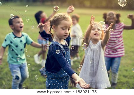 Group of kindergarten kids friends playing blowing bubbles fun