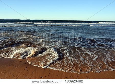 Tropical beach in the sun beach background scene with clear blue sky and waves rolling on the beach. White foam on beach water nature. Summertime blue sea and waves yellow sun and sand.