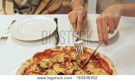 Girl cuts a pizza for two friends.
